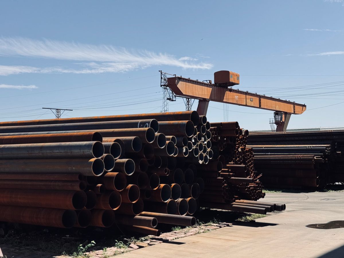 Rolled steel stock stacked in a mill yard under a gantry crane
